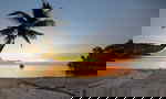 A lone boat sits in the water on a deserted beach at sunset