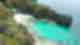 Aerial shot of rocky grey cliffs covered in green jungle with bright turquoise waters and traditional boats