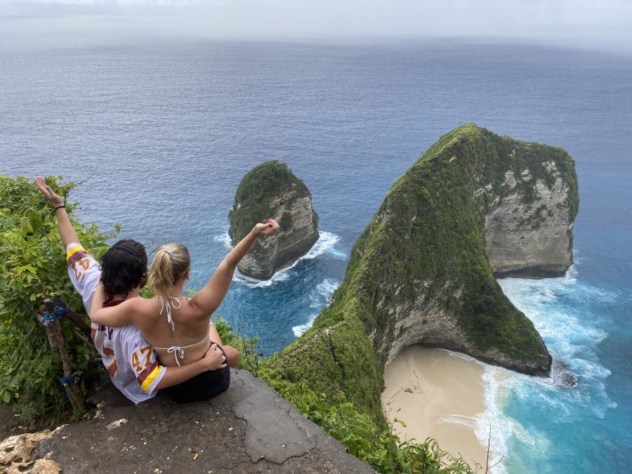 Travellers at Kelingking viewpoint looking out with their hands in the air.