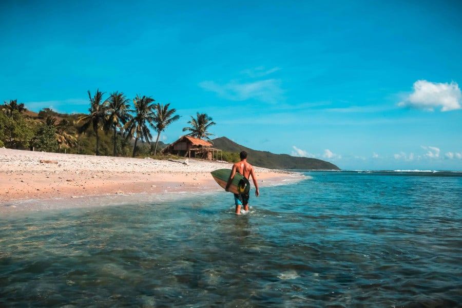 Traveller with surf board in Lombok walking out of the water